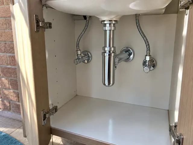 Neat under-sink plumbing with chrome trap and open cabinet doors in Lalor Park